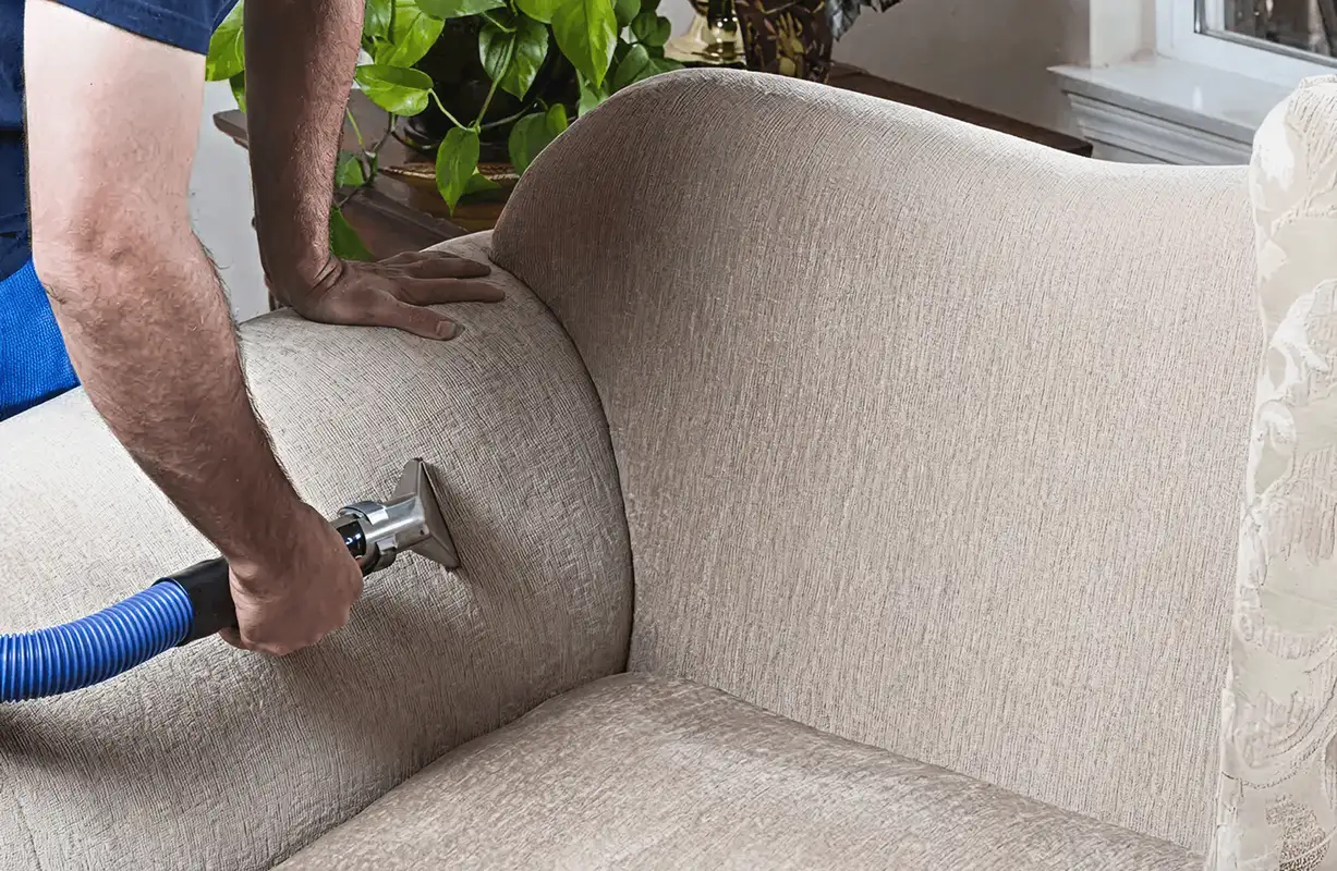 Professional upholstery cleaner deep-cleaning a fabric sofa with a handheld extraction tool and hose, Pittsburgh, PA.